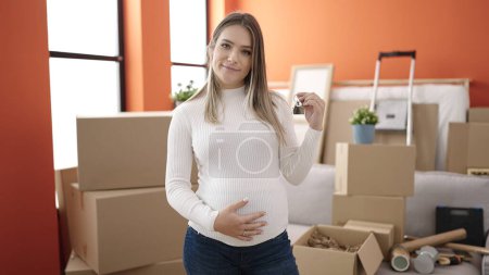 Photo for Young pregnant woman touching belly holding keys at new home - Royalty Free Image