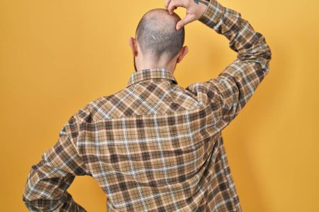 Téléchargez les photos : Young hispanic man with tattoos standing over yellow background backwards thinking about doubt with hand on head - en image libre de droit