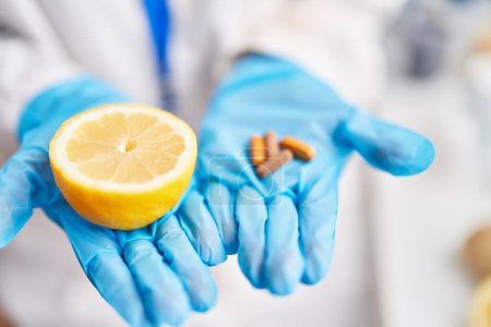 Téléchargez les photos : Jeune femme blonde scientifique tenant citron moyen et pilules au laboratoire - en image libre de droit