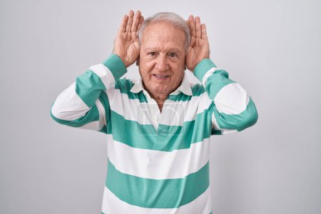 Photo for Senior man with grey hair standing over white background doing bunny ears gesture with hands palms looking cynical and skeptical. easter rabbit concept. - Royalty Free Image