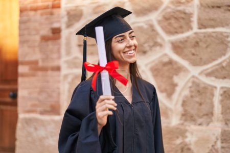 Photo for Young hispanic woman wearing graduated uniform holding diploma at university - Royalty Free Image