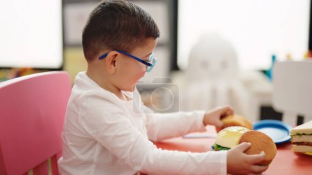 Téléchargez les photos : Adorable garçon hispanique jouant avec jouet hamburger à la maternelle - en image libre de droit