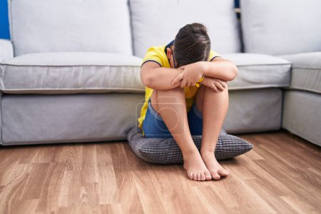 Foto de Adorable niño hispano estresado sentado en el suelo en casa - Imagen libre de derechos