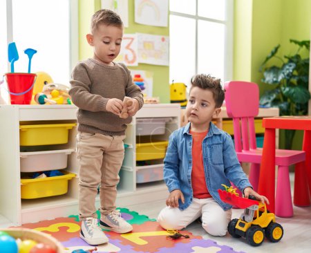 Téléchargez les photos : Adorables garçons jouant avec tracteur et jouet de dinosaure assis sur le sol à la maternelle - en image libre de droit