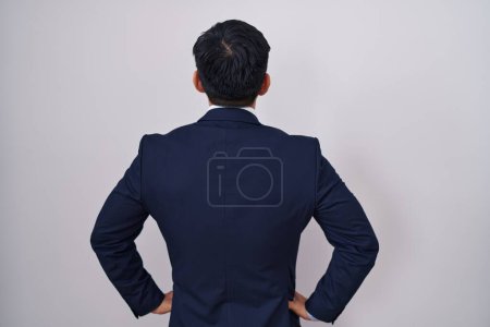 Foto de Joven asiático hombre vistiendo traje de negocios y corbata de pie hacia atrás mirando hacia otro lado con brazos en el cuerpo - Imagen libre de derechos