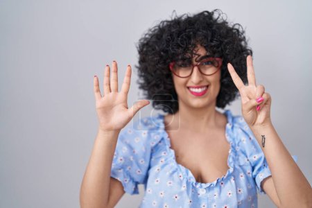 Photo for Young brunette woman with curly hair wearing glasses over isolated background showing and pointing up with fingers number seven while smiling confident and happy. - Royalty Free Image