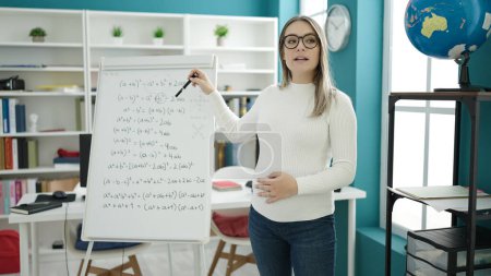 Photo for Young pregnant woman teaching maths on magnetic board touching belly at classroom - Royalty Free Image
