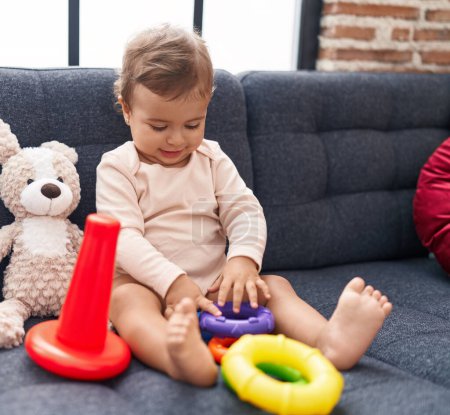 Foto de Adorable bebé hispano jugando con aros juego sentado en el sofá en casa - Imagen libre de derechos