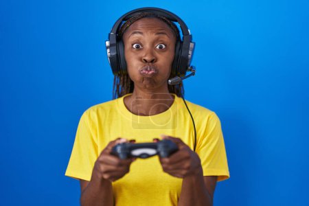 Photo for African american woman playing video games puffing cheeks with funny face. mouth inflated with air, catching air. - Royalty Free Image