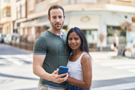 Foto de Hombre y mujer interracial pareja abrazándose unos a otros usando smartphone en la calle - Imagen libre de derechos