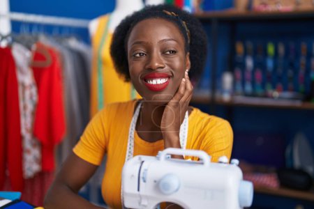 Foto de Mujer afroamericana sastre sonriendo confiado usando máquina de coser en estudio de costura - Imagen libre de derechos