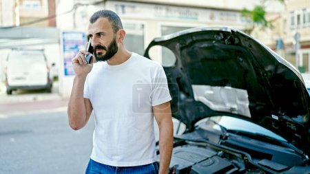 Foto de Joven hispano hablando en smartphone con seguro para avería de coche en la calle - Imagen libre de derechos