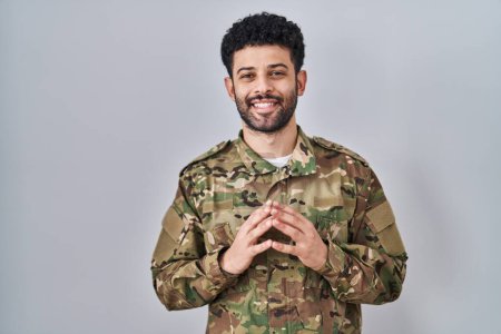 Téléchargez les photos : Homme arabe portant des mains uniformes de l'armée de camouflage ensemble et les doigts croisés souriant détendu et joyeux. succès et optimisme - en image libre de droit