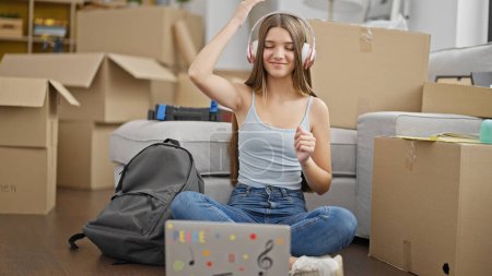 Photo for Young beautiful girl student listening to music sitting on floor dancing at new home - Royalty Free Image
