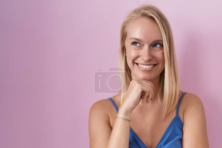 Téléchargez les photos : Jeune femme caucasienne debout sur fond rose avec la main sur le menton penser à la question, expression coûteuse. Visage souriant et réfléchi. concept de doute. - en image libre de droit