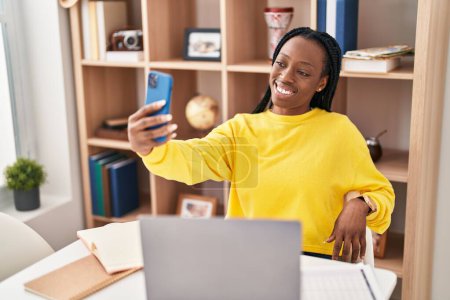 Téléchargez les photos : Femme afro-américaine utilisant un ordinateur portable faire selfie par smartphone à la maison - en image libre de droit