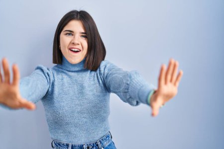 Téléchargez les photos : Jeune femme hispanique debout sur fond bleu faisant geste d'arrêt avec les paumes des mains, expression de colère et de frustration - en image libre de droit