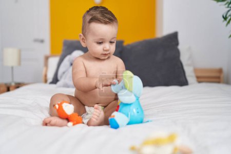 Foto de Adorable bebé caucásico jugando con un juguete de elefante sentado en la cama en el dormitorio - Imagen libre de derechos