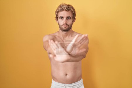 Téléchargez les photos : Homme caucasien debout torse nu portant écran solaire expression de rejet croisement bras et paumes faisant signe négatif, visage en colère - en image libre de droit