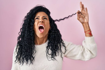 Téléchargez les photos : Moyen Age femme hispanique tenant les cheveux bouclés en colère et fou hurlant frustré et furieux, criant avec colère levant les yeux. - en image libre de droit