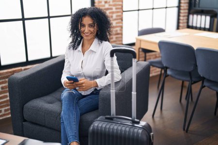 Téléchargez les photos : Young hispanic woman business worker using smartphone waiting for travel at office - en image libre de droit