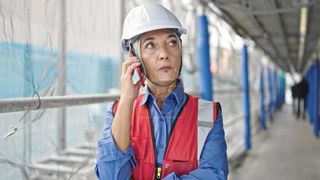 Téléchargez les photos : Moyen âge femme aux cheveux gris constructeur parler sur smartphone à la rue - en image libre de droit