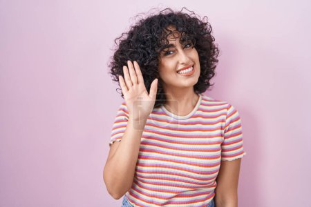 Foto de Joven mujer de Oriente Medio de pie sobre fondo rosa renunciando a decir hola feliz y sonriente, gesto de bienvenida amistoso - Imagen libre de derechos