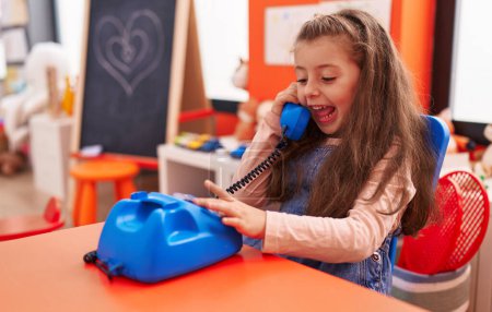 Photo for Adorable hispanic girl playing telephone toy sitting on table at kindergarten - Royalty Free Image