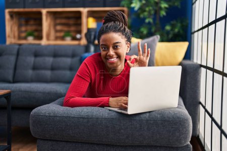 Photo for Young african american with braids working using computer laptop doing ok sign with fingers, smiling friendly gesturing excellent symbol - Royalty Free Image