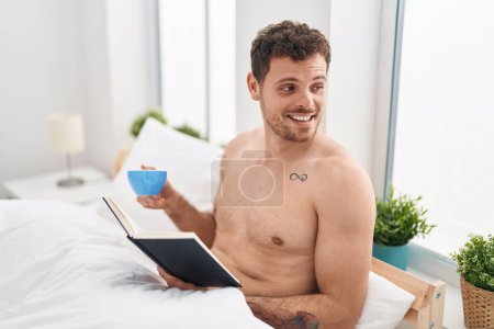 Photo for Young hispanic man reading book and drinking coffee sitting on bed at bedroom - Royalty Free Image