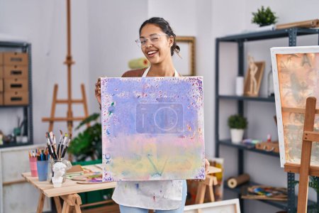 Foto de Mujer brasileña joven sosteniendo el lienzo del pintor en el estudio de arte guiño mirando a la cámara con expresión sexy, cara alegre y feliz. - Imagen libre de derechos