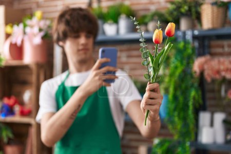 Foto de Joven florista hombre rubio hacer foto para florecer por teléfono inteligente en la tienda de flores - Imagen libre de derechos