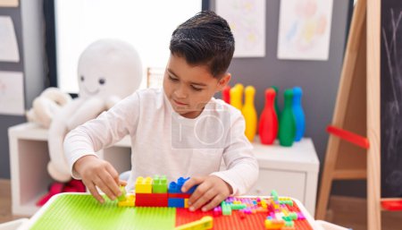 Téléchargez les photos : Adorable garçon hispanique jouant avec des blocs de construction assis sur la table à la maternelle - en image libre de droit