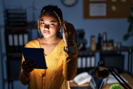 Téléchargez les photos : Femme afro-américaine avec des tresses travaillant au bureau la nuit avec une tablette faisant geste italien avec la main et les doigts expression confiante - en image libre de droit