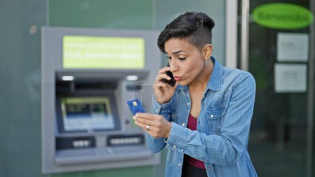 Téléchargez les photos : Jeune belle femme hispanique argumentant sur smartphone tenant la carte de crédit au guichet de la banque - en image libre de droit