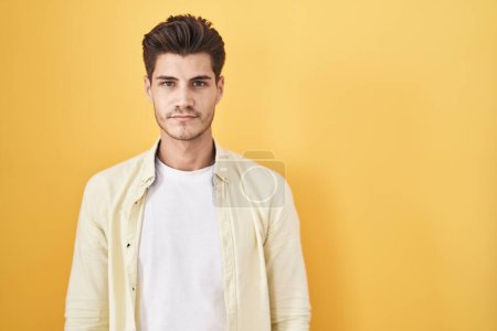 Photo for Young hispanic man standing over yellow background relaxed with serious expression on face. simple and natural looking at the camera. - Royalty Free Image