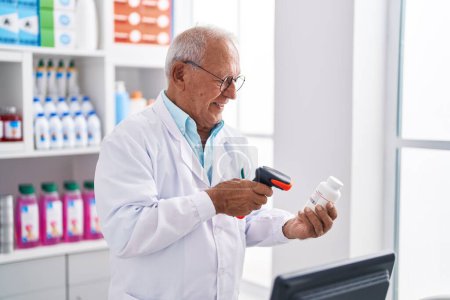 Foto de Senior grey-haired man pharmacist scanning pills bottle at pharmacy - Imagen libre de derechos