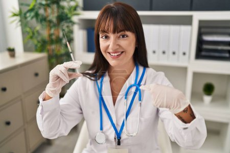 Photo for Young brunette doctor woman holding syringe pointing finger to one self smiling happy and proud - Royalty Free Image