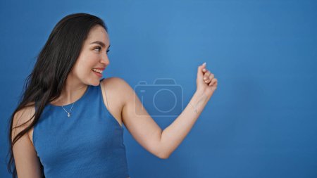 Foto de Joven hermosa mujer hispana sonriendo confiada mirando hacia un lado sobre un fondo azul aislado - Imagen libre de derechos