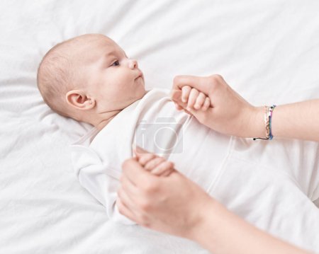 Téléchargez les photos : Adorable bébé caucasien couché sur le lit tenant les mains de la mère à la chambre - en image libre de droit