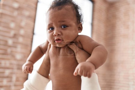 Téléchargez les photos : Bébé afro-américain relaxant sur les mains de la mère à la maison - en image libre de droit