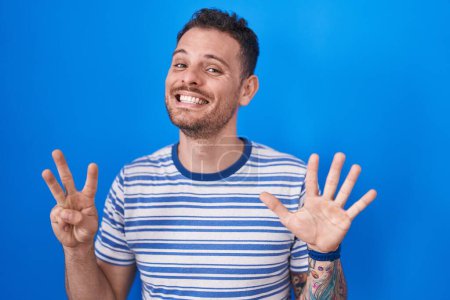 Foto de Young hispanic man standing over blue background showing and pointing up with fingers number eight while smiling confident and happy. - Imagen libre de derechos