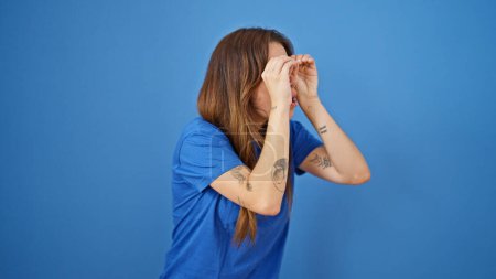 Foto de Joven mujer hispana hermosa haciendo gesto de prismáticos con las manos buscando sobre fondo azul aislado - Imagen libre de derechos