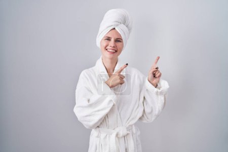 Téléchargez les photos : Blonde femme caucasienne portant peignoir souriant et regardant la caméra pointant avec deux mains et doigts sur le côté. - en image libre de droit