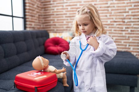 Photo for Adorable blonde girl playing doctor with baby doll at home - Royalty Free Image