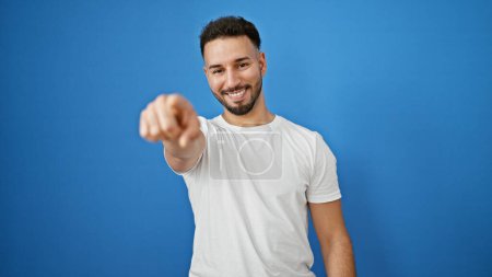 Téléchargez les photos : Jeune homme arabe à la recherche de quelqu'un pointant du doigt vers la caméra sur fond bleu isolé - en image libre de droit