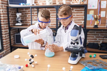 Foto de Adorable chicos estudiante vertiendo líquido en tubo de ensayo en el aula de laboratorio - Imagen libre de derechos