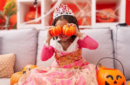 Téléchargez les photos : Africaine américaine fille portant costume princesse tenant citrouilles sur les yeux à la maison - en image libre de droit