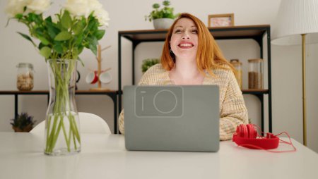 Téléchargez les photos : Young redhead woman using laptop sitting on desk at home - en image libre de droit