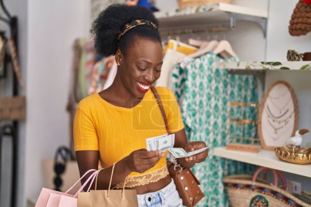 Foto de Mujer afroamericana cliente sosteniendo bolsas de compras contando dólares en tienda de ropa - Imagen libre de derechos